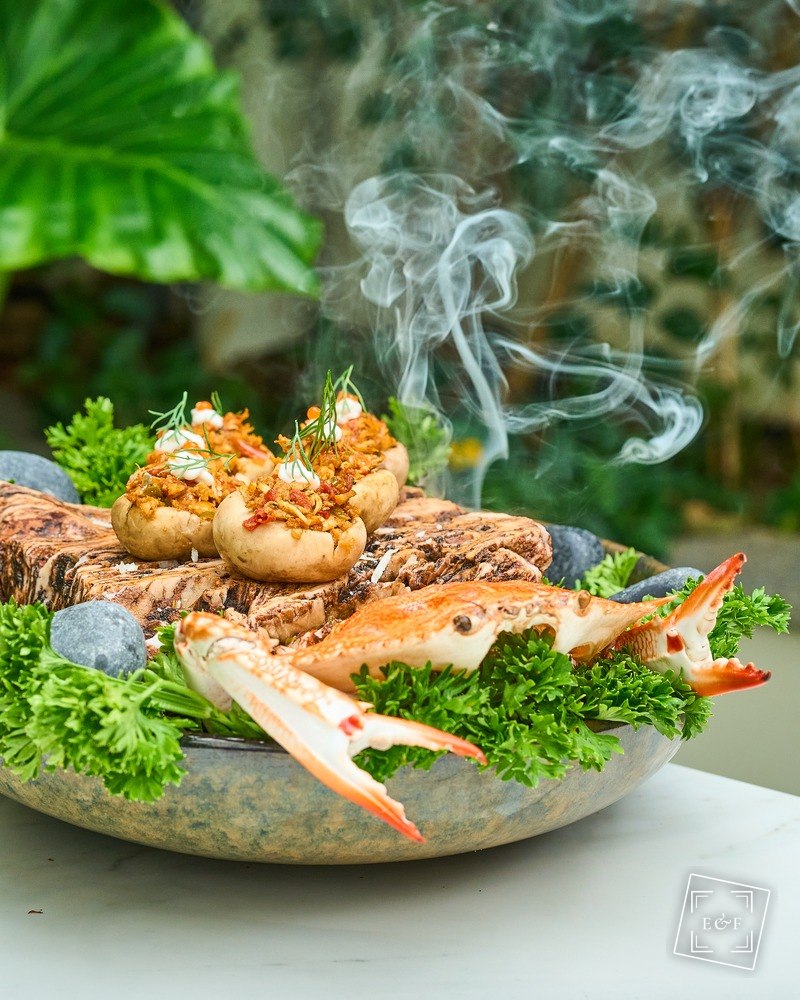 Blue crab and stuffed mushrooms plated over herbs with rising steam